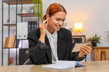 Merkez ofisteki genç iş kadını akıllı telefonuyla internet yayınını dinliyor. Kulaklıklarıyla not defterinde fikirleri yazıyor. Masadaki serbest çalışan kız para biriktirmek ve servetini arttırmak için yararlı tavsiyeler yazıyor.