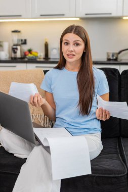 Dizüstü bilgisayardaki genç kadın mali evrakları kontrol ediyor faturaları görüyor ve kafası çok karışık. Kanepedeki beyaz kız kameraya bakıyor. Aile bütçesini kontrol ediyor. Faturalar da sorunu bulup düzeltmeye çalışıyor..