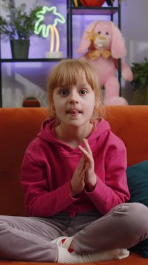 Çocuk kız başarıyı kutluyor diye bağırıyor. Gol başarısı, iyi haber, el kol hareketi. Başardım, piyango şansı. Genç bir kız evde oyun oynuyor oturma odasında kanepede oturuyor..