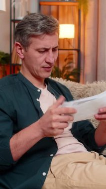 Evdeki genç adam görünür bir şekilde stresli ve gerginken faturaları kanepeye fırlatıyor. Kafkasyalı adam beklenmedik mali sorunlara ve yüksek aylık harcamalara tepki verirken hayal kırıklığı ve öfke belirtileri gösteriyor.