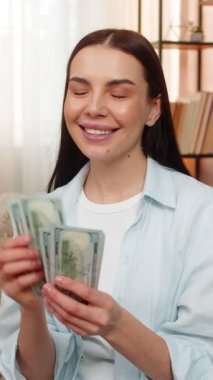 Evde para sayan genç bir kadın maaş ya da gelir aldıktan sonra mutlu bir şekilde gülümsüyor. Kanepede oturan beyaz kız mutluluğu, maddi ödülü, olumlu para duygusunu yaşıyor.