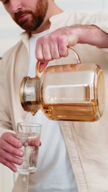 Orta yaşlı bir adam, ev mutfağındaki bardağa temiz su dökerek sağlıklı beslenmeden memnun olur. Genç çocuk evde antrenman yaptıktan sonra kilo vermek için saf su içer.