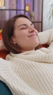 Yorgun genç bir kadının portresi evdeki kanepede dinlenmenin keyfini çıkarıyor. Mutlu güzel bayan kanepede dinleniyor yorucu bir günün ardından kestiriyor, gözlerini kapatıyor, ellerini başının arkasına koyuyor, stresten kurtuluyor, dinleniyor.