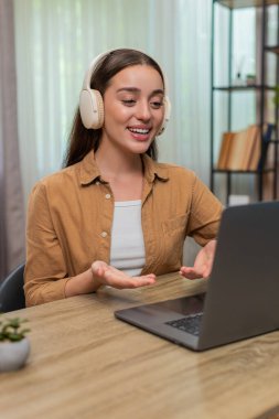 Evdeki masada oturan genç bir kadın kablosuz kulaklık takıyor ve dizüstü bilgisayarda konuşuyor ve destek veriyor. Beyaz kız ciddi ses tonlarını sakince müşterilere yararlı cevaplar vererek koruyor.