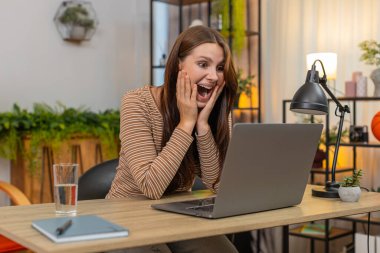 Evde dizüstü bilgisayara bakan genç bir kadın yüksek proje derecesi görüyor. Hayret verici bir şekilde gülüyor ve yanakları tutuyor. Masa başındaki beyaz kız olumlu eleştiri yazar. Teşekkürler mesajı yazar ve başarıyı ruh haliyle kutlar.