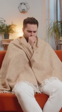 Evdeki oturma odasında kanepede otururken battaniyeyle kaplanmış hasta, beyaz bir erkek. Adam nezle, virüs ya da grip olmuş. Yorgun adam kendini kötü hissediyor ve bronşiti, tıbbi sorunları ve astımı var..