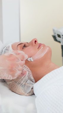 Enzyme therapy. Beautician applying moisturizing medical peeling cream mask on young woman face with brushes. Girl skincare procedure on spa. Facial cosmetology treatment. Natural cosmetic products