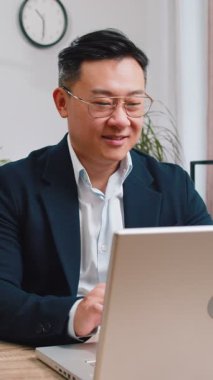 Ev işyerinde bilgisayarla çalışan Asyalı mutlu iş adamının portresi. Yönetici Çinli, resmi takım elbiseli olgun bir adam defter üzerinde çalışıyor. Mesaj gönderiyor, internetten alışveriş yapıyor.