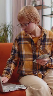 Planlama bütçesi. Zengin, mutlu, genç bir kadın para sayıyor dizüstü bilgisayar kullanıyor. Kanepede oturan faturaları hesaplıyor. Kazancından memnun bir bayan, planlı tatil için para biriktiriyor, hediyeler.