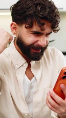 Evdeki Hintli adam piyangoyu kazanmakla ilgili akıllı telefon e-postalarını okuyor online oyunda kazanmakla ilgili gülümsemeler nakit ikramiyesi hakkında mutlu. Kanepedeki Arap adam turuncu cep telefonundaki başarı mesajını kutluyor.