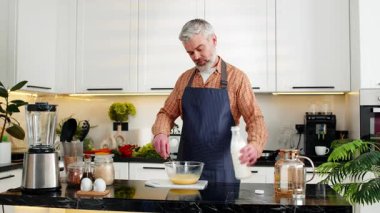 Sağlıklı yemek hazırlığı için mutfak tezgahında omlet yumurtası çırparken orta yaşlı bir adam gülümsüyor. Olgun adam evde yemek yapmayı seviyor. Sağlıklı ve kilolu olmak için diyet kahvaltısı seçiyor..