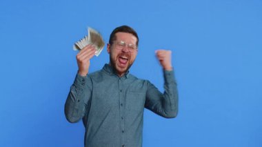 Zengin, mutlu, orta yaşlı, gözlüklü, mutlu bir beyaz adam. Bir hayran, başarılı bir iş adamı, piyango talihlisi, büyük gelir getiren banknotlar sallıyor. Mavi arkaplanda izole edilmiş adam