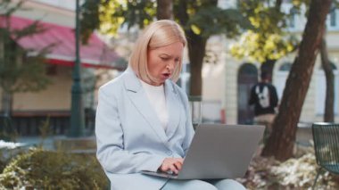 Yetişkin bir iş kadınının dizüstü bilgisayarından kötü haberler okuması şehir caddesinde bankta oturması. Resmi takım elbiseli sinirli bayan işveren rahatsız edici bir ihbar aldı ve endişe içinde olumsuz mesaja baktı..