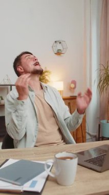 Zengin beyaz adam büyük kar elde ediyor piyango parası kazanıyor alışveriş yaparak yağmur yağıyor. Ev ofisinin masasında dizüstü bilgisayarını yumruklayan genç, serbest çalışan adam yöneticisi. Dikey.