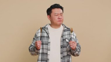 Yemek hazır. Aç Asyalı orta yaşlı orta yaşlı bir adam, elinde çatal bıçakla yemek servisi yapmayı bekliyor. Bej arka planda lezzetli bir restoran yemeğini takdir edecektir.