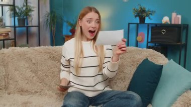 Kafkasyalı gülümseyen heyecanlı kadın evinde oturmuş piyangoyu kutluyor elinde bilet ve para var. Neşeli bir şekilde kameraya bakarak rahatlamak eğlenceli ve mutlu olmak.