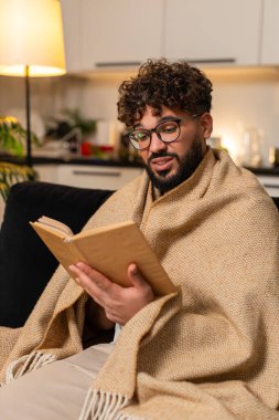 Evde gözlüklü, battaniyeye sarılı Arap bir adam en sevdiği kitabı okuyor. Yavaş sayfa nefesini kesiyor. Kanepedeki Mısırlı adam sessiz bölüm gülüşlerini sever. Gece geç saatlerde kitap ayracı sıcak, rahat bir ruh hali tutar..