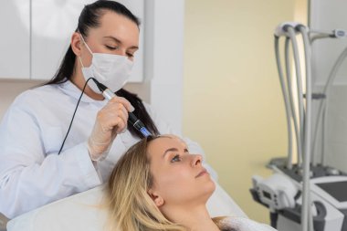 Alopecia. Kadın saç dökülmesi tedavisi. Trikoloğun kozmetik doktoru kafa derisi dermapen fraksiyonel mikronedle, klinik mezoterapisi üzerine şırıngadan vitamin serumu enjekte ediyor..