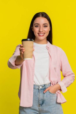 Elinde kağıt kahve fincanı tutan genç bir kadın derin bir nefes alıyor tatmin olmuş bir gülümsemeyle rahatlatıcı bir koku. Sarı arka planda izole edilmiş bir kız sıcak kahveden duygusal zevk aldığını gösterir.