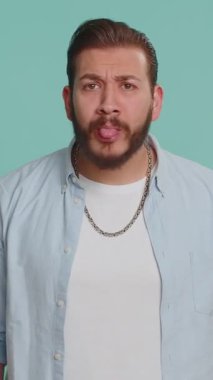 Komik, komik, genç Lübnanlı bir adam şakacı, aptal yüz ifadeleri yapıyor, suratını buruşturuyor, aylak aylak dolanıyor, dil gösteriyor. Stüdyonun mavi arka planında izole edilmiş yakışıklı çılgın Arap çocuk.