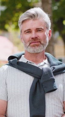 Mutlu sakallı, olgun bir adamın portresi. Dostça gülümseyen, kameraya bakan mutlu yüz ifadesi. Hayal kuran, dinlenen, rahatlayan. Şehir Güneşi Sokağı arka planındaki adam.