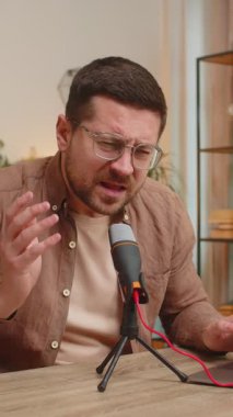 Genç, beyaz, gözlüklü bir blog yazarı mikrofona şarkı söylerken dizüstü bilgisayar kullanıyor ve eliyle ritmik hareketler yapıyor. Oturma odasında oturuyor..