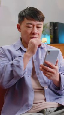 Kanepede oturan Asyalı adam evde otururken cep telefonuyla gülümsüyor. Çinli yetişkin bir çocuk akıllı telefon sosyal medya uygulamalarından mesajlarını paylaşıyor, rahatlama filmi izliyor.