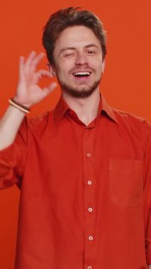 - Tamam. Mutlu beyaz adam kameraya onaylayıcı bir şekilde bakıyor. Pozitif geri bildirim veriyor. Zafer göz kırpma flörtünü kutlamak için güzel bir şey onaylıyor. Turuncu arka plandaki genç adam.