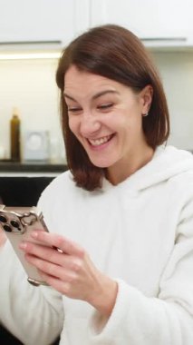 Evde genç bir kadın telefonda finans uygulaması kullanıyor. Denge yükseliyor. Kazanan yumruğunu kaldırıyor. Kanepede oturan beyaz kız telefon notlarında yeni bir hedef belirledi..