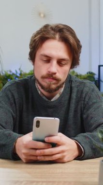 Masada oturan beyaz adam ofis odasındaki dairede cep telefonu tebessümleri kullanıyor. Genç sakallı adam akıllı telefon sosyal medya uygulamaları üzerinden rahatlama filmi izlerken mesajları paylaşıyor.