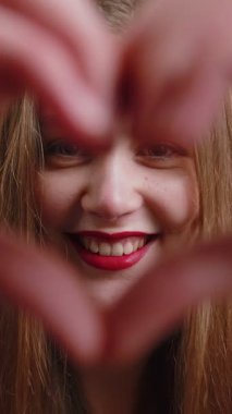 Ben de seni seviyorum. Oturma odasındaki kanepede oturan mutlu genç bir kadın aşkın sembolünü yapar. Kameraya kalp işaretini gösterir. Romantik duygular samimi olumlu duygular ifade eder. Sadaka, minnettarlık, bağış.