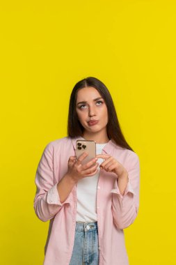 Genç bir kadın akıllı telefondan sosyal medyayı besliyor. Sinirli ve sıkılmış bir ifadeyle gözleri yuvarlanıyor. Sarı arka plandaki kız açıkça tekrarlanan içeriğe karşı olumsuz tepki gösteriyor.