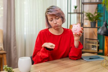 Mutsuz genç bir kadın, kumbaradaki bozuk paraları sayıyor evde oturmuş, hayal kırıklığına uğramış bir şekilde iç çekiyor. Finansal sıkıntı ve hayal kırıklığı gösteren beyaz bir kız yetersiz tasarruf konusunda endişeli..