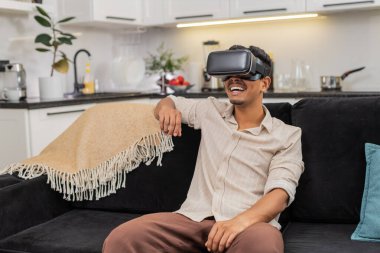 Evde oturan Hintli adam VR kulaklık takıyor. Vay be, film izliyor ve sanal sinemayı ilgiyle keşfediyor. Kanepedeki Arap adam internet içeriği hakkında konuşuyor. Kısa kelimeler söylüyor. Kafa sallıyor ve sakin hareket ediyor.