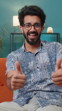 Gibi. Mutlu heyecanlı Hintli adam onaylayıcı bir şekilde kameraya bakıyor, olumlu bir şey gösteriyor, iyi haber, olumlu geri bildirim gibi. Genç Hindu çocuk evdeki kanepede oturuyor.