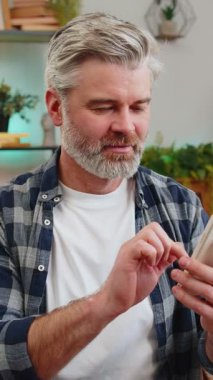 Evdeki koltukta oturan mutlu, olgun bir adam akıllı telefon kullanan eski bir dostundan mesaj alıyor. Gülümseyerek yüzünü yana çevir. Beyaz saçlı, yaşlı bir adam evdeki oturma odasında telefon ekranından iyi haberler okuyor..