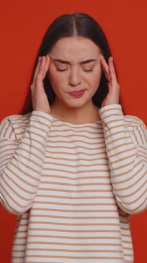 Hipster young pretty woman in pullover rubbing temples to cure headache problem, suffering from tension, migaine, stress, grimacing in pain, high blood pressure isolated alone on red wall background