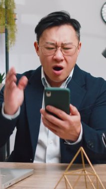 Asyalı işadamı serbest çalışan akıllı telefon daktilo kullanıyor, beklenmedik piyango sonuçlarını kaybediyor, kötü haber, servet kaybı, ofis çalışma masasında başarısız olma. Takım elbiseli Çinli bir erkek.