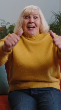 Kanepe oturma odasında heyecanlı yaşlı bir kadın TV 'de ilginç bir spor oyunu izliyor, sosyal medya içerikli çevrimiçi bir film çekiyor. Yaşlı emekli eğleniyor.