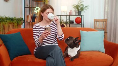 Orta yaşlı bir kadın evde Fransız buldoguyla kahve içiyor. Akıllı telefondan haberleri okuyor. Sakin ve mutlu hissediyor. Kız evcil köpek kanepeye oturmuş gülümsüyor. Kupanın keyfini çıkarıyor. Sabah haberlerine bakıyor. Günlük yaşam tarzını internette tarıyor.