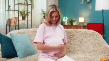 Hamile, orta yaşlı bir kadın karnının üzerinde elleri ile kalp oluşturur. Yavaşça gülümser ve doğum için beklenti hisseder. Kafkasyalı kız kanepeye uzanmış, nazik bir anın tadını çıkarıyor. Yakında bebeğe sessiz bir aşk yolluyor..