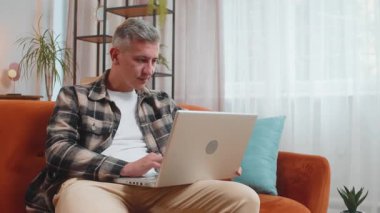 Aman Tanrım. Vay canına. Gri saçlı beyaz adam dizüstü bilgisayar kullanıyor, iyi haber mesajı alıyor, ani zaferi kutluyor, galibiyeti kutluyor, evinde online alışveriş yapıyor koltukta oturuyor.