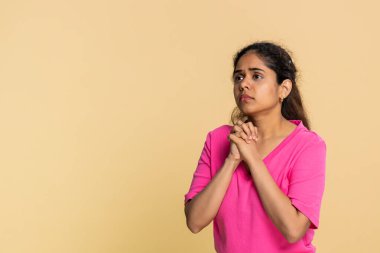 Hintli kadın dua ederken el ele tutuşur, umut dolu samimi bir ifadeyle yukarıya bakar. Bej arka plandaki Arap kız açıkça gerçek bir dua, inanç, umut, ciddi bir arzu gösteriyor.