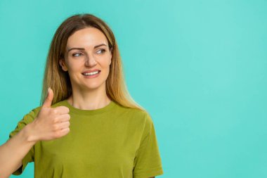 Orta yaşlı bir kadın, güçlü bir destek, uzlaşma ya da sonuçtan veya mesajdan memnuniyet gösteren parlak bir gülümsemeyle baş parmağını kaldırır. Mavi arka planda izole edilmiş bir kız pozitifliğini ve onay jestini gösterir