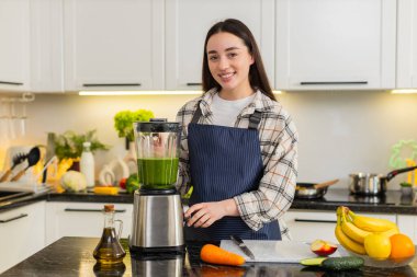 Kadın yeşil smoothie 'yi ıspanak, elma, muz ve havuçla karıştırmak için mutfak tezgahına blender koyuyor. Sağlıklı ev yapımı detoks içeceği konsepti diyet beslenme ve sağlıklı yaşam için, kız taze kahvaltı hazırlıyor..
