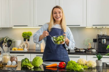 Orta yaşlı bir kadın evde mutfaktaki online izleyiciler için bir kase sebze salatası ve video kayıt tarifi gösteriyor. Genç kız keto vejetaryen beslenme ve sağlıklı yaşam tarzı hakkında podcast yapıyor..