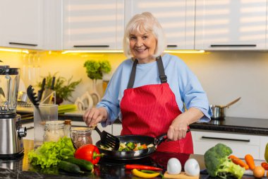 Sağlıklı beslenme hedeflerini korurken kıdemli yaşlı kadın mutfakta sebze kızartıyordu. Yaşlı büyükannem evde besleyici yemekler hazırlar sağlık yaşam tarzı için dengeli beslenme için..