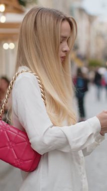 Gezgin, sarışın, akıllı telefon kullanarak açık hava mobil navigatör uygulamasında haritada arama yapmak için kısa mesajlar yazan genç bir kadın. Kentin arka sokaklarından genç bir bayan geçiyor.