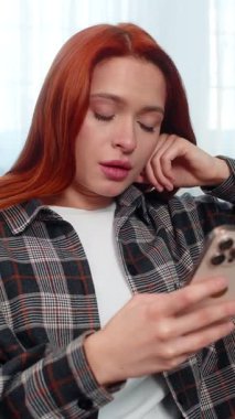 Evde elinde akıllı telefon olan genç bir kadın kötü haberden sonra üzgün bir suratla ekrana bakıyor. Kanepedeki beyaz saçlı kız üzgün hissediyor, mesajlara duygusal tepki veriyor ya da beklenmedik sonuçlar veriyor.