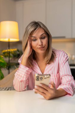 Akşamları evde yetişkin bir kadın akıllı telefondan gelen haberlerde sıkılmış yorgun ağır gözler stres hisseder. Akşamları masadaki beyaz kız yemek okuyor kaşlarını çatıyor, nefes alıyor sakin bir motivasyon arıyor..